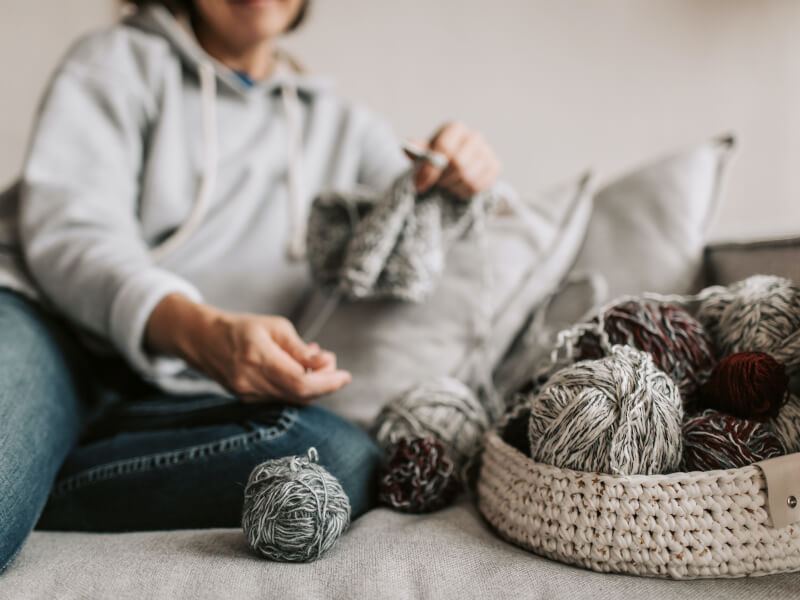 a person sits on a sofa knitting with balls of yarn next to them